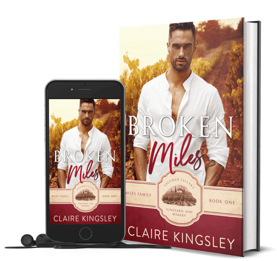 The book cover for Broken Miles, a small-town romance by Claire Kingsley, is an image of a dark haired man in a white button down shirt standing in a vineyard with the sun setting in the background. He has his hands tucked into his pockets and a serious expression on his face. There are shades of dark red and white. Next to the book is a phone showing the cover with a pair of wired earbuds.