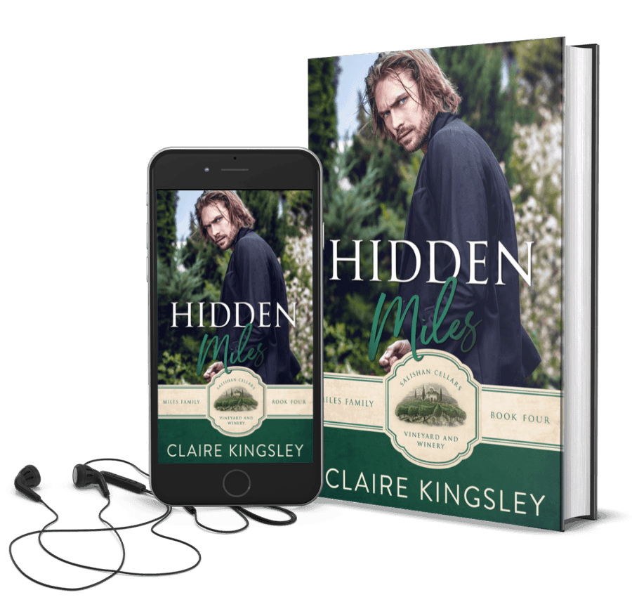 The book cover for Hidden Miles, a small-town romance by Claire Kingsley, is an image of a man in a black coat with long dark hair turned looking over his shoulder with a furrowed brow, a forest of trees in the background. There are shades of green and white. Next to the book is a phone showing the cover with a pair of wired earbuds.