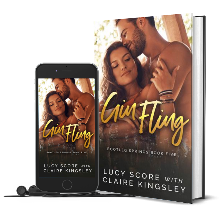 The book cover of Gin Fling, a novel by Lucy Score with Claire Kingsley, is an image of a dark haired woman wrapped in the arms of a bearded man with her back to his front, his face pressed to her forehead. Next to the book is a phone showing the cover with a pair of wired earbuds.