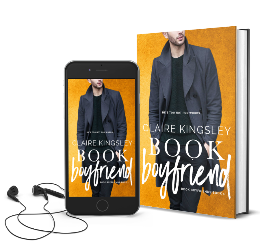 The book cover for Book Boyfriend, a novel by Claire Kingsley, is an image of a bearded man wearing a collared coat standing with his hands tucked into the pockets of his black pants. He is on a yellow background. Next to the book is a phone showing the cover with a pair of wired earbuds.