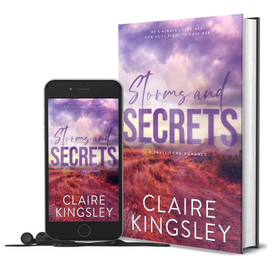 The book cover for Storms and Secrets, a small-town romance by Claire Kingsley, is a landscape photograph of a field of eerie tall grass in shades of reds and orange below a cloudy purple sky with mountains in the distance. Next to the book is a phone showing the cover with a pair of wired earbuds.